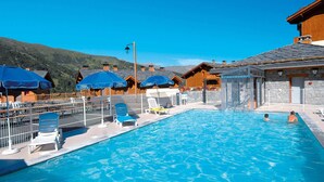 A swimming pool with lounge chairs and umbrellas, wooden buildings, and a mountainous backdrop. - Family & Pet-friendly Base (Valmeinier)