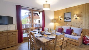 A wooden-paneled room with a dining table set for four, a sofa with cushions, a television, and a window with curtains. - Family & Pet-friendly Base (Valmeinier)
