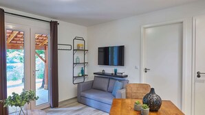 A living room with a sofa, a TV mounted on the wall, a wooden table with decorative items, and a sliding glass door leading to an outdoor area. - Holiday Home in Mauroux With Pools & Vineyards (Mauroux)