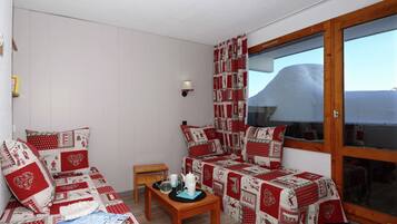A cozy room with a bed, a small table with a kettle and cups, and a window with a view of a mountain.
