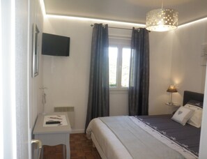 A bedroom with a bed, bedside table, lamp, and a window with curtains. - Sea View Family Escape (Port-Bail-sur-Mer)