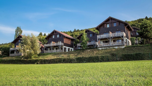 Reihenweise Chalets mit Balkonen, gelegen an einem Hang mit einer grünen Wiese im Vordergrund.