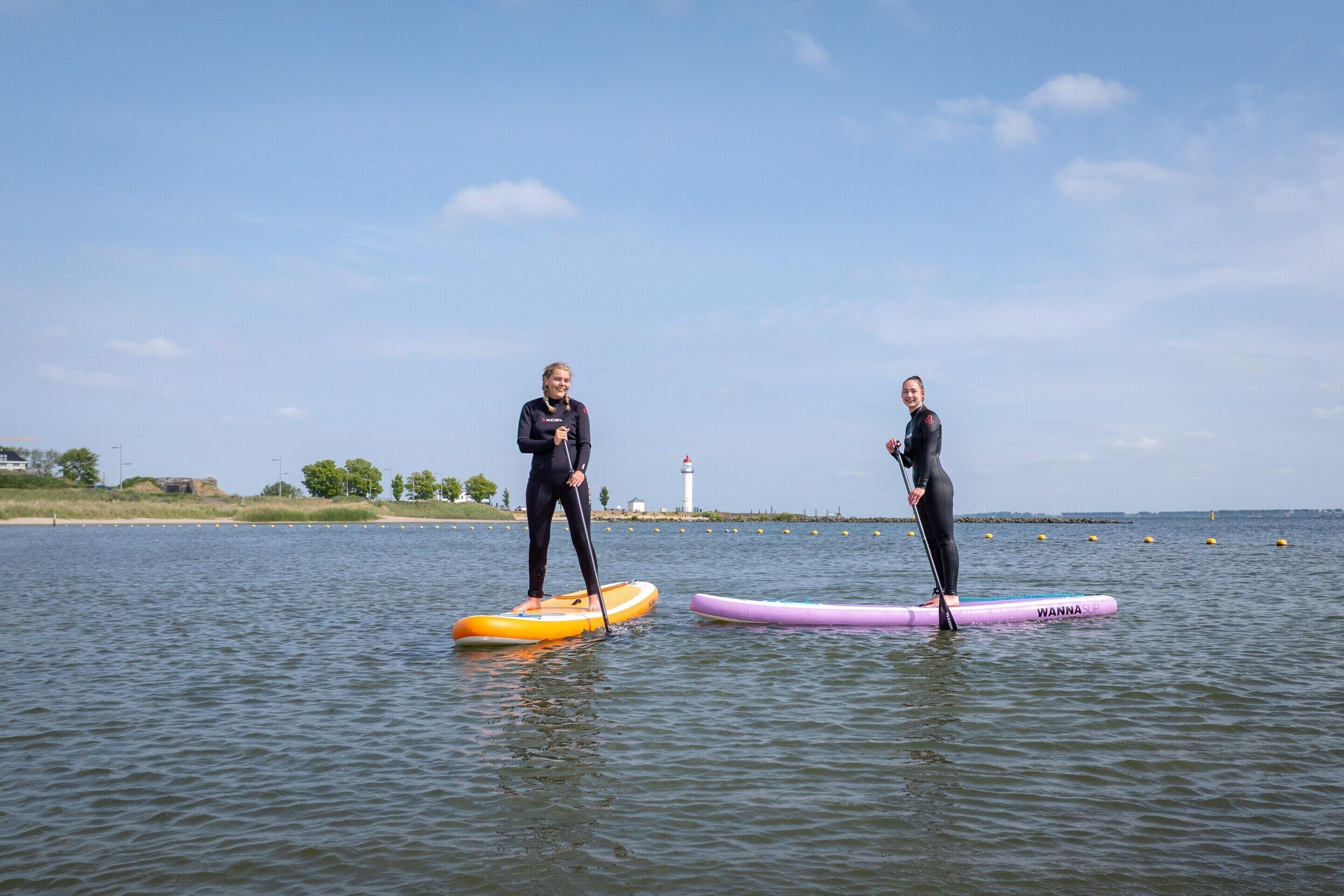 Two people on paddleboards in a calm body of water with a lighthouse in the background.