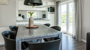 A modern kitchen with white cabinets, a central island, and a large window. - Cozy Chalet With Dishwasher in Noordwijk, Near the Sea (Noordwijk)