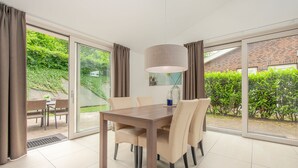 A dining area with a table and chairs, large windows, and a view of greenery outside. - Modern Bungalow With Washer (Arcen)