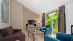 A modern living room with a sofa, armchair, coffee table, and TV. - Modern Bungalow With Washer (Arcen)