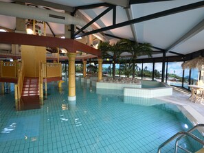 En indendørs swimmingpool med fliset gulv, en træt rutsjebane og et tag af strå.