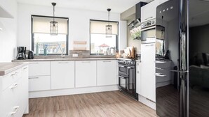 A modern kitchen with white cabinets, a black refrigerator, a stove, and two pendant lights. - Holiday Home With Private Jetty on Water (Akkrum)
