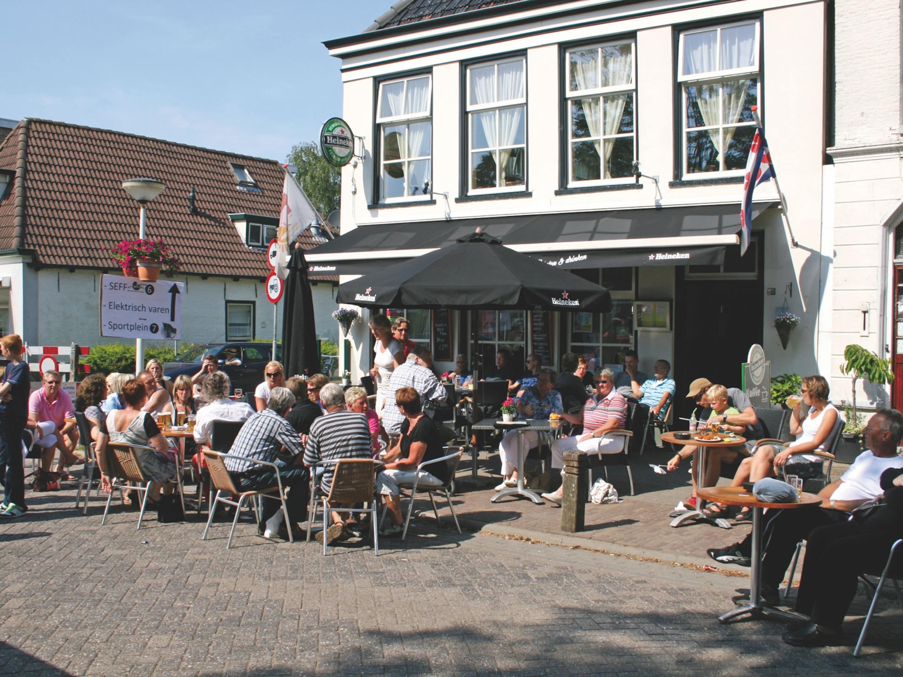An outdoor seating area with tables and chairs, a building with a signboard, and a flag.