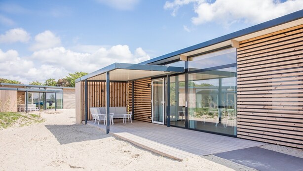 Una moderna casa sulla spiaggia con veranda in legno, porte scorrevoli in vetro e posti a sedere esterni.