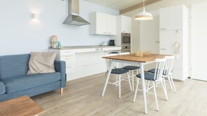 Una cucina moderna con mobili bianchi, soffitto in legno e zona pranzo con tavolo in legno e sedie bianche.