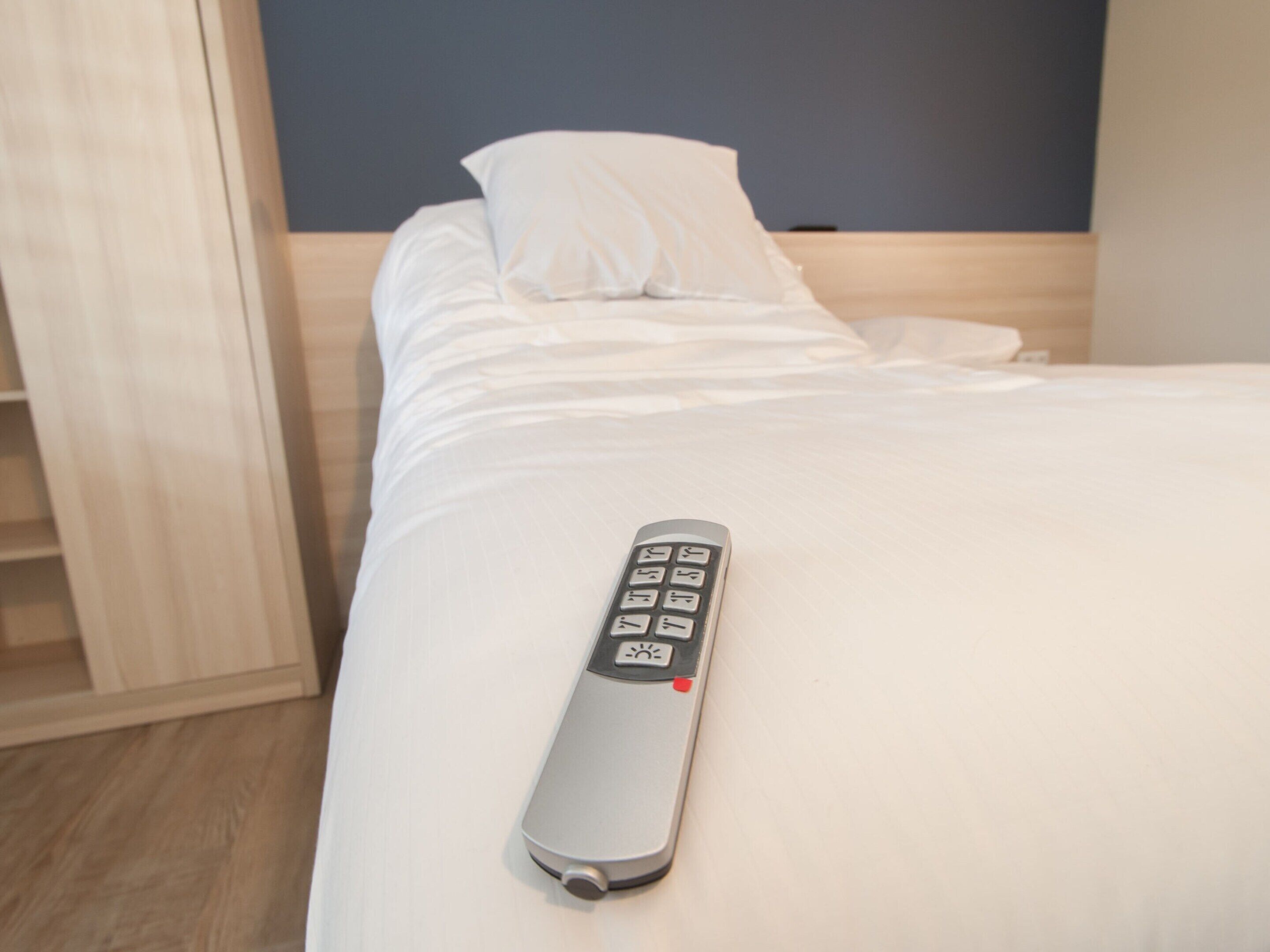 Ein Bett mit weißen Laken und einer Fernbedienung darauf.