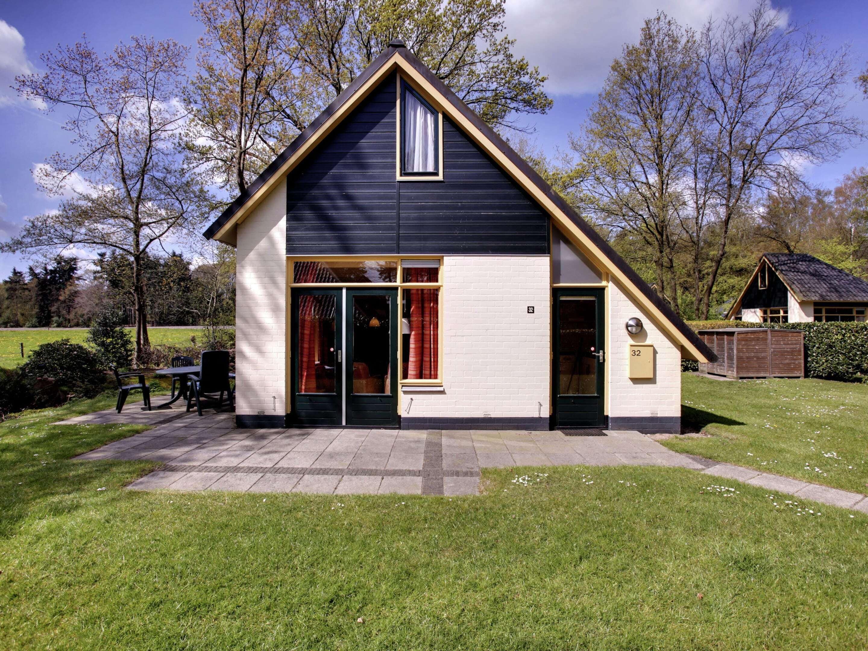 A two-story house with a gabled roof, a front door, and a small porch with chairs.