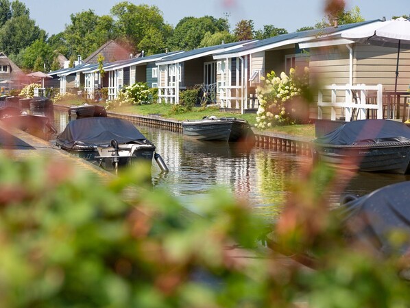 A canal with boats and a row of houses with a covered walkway. - Sunny Giethoorn Cottage (Giethoorn)