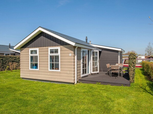 Une maison de plain-pied avec un toit en pente, une terrasse dotée de mobilier d’extérieur et une pelouse bien entretenue.