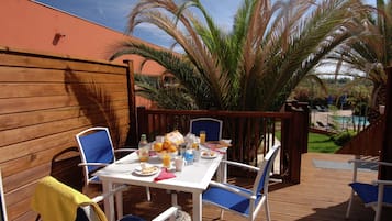 An outdoor patio with a table set for breakfast, surrounded by chairs, and palm trees in the background.