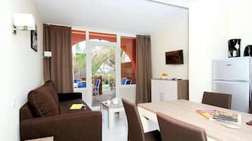 A room with a sofa, a dining table with chairs, a refrigerator, a television, and a window with curtains.