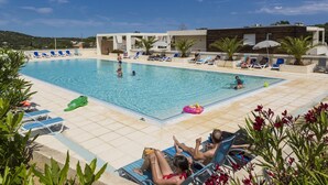 Ein Swimmingpool mit Liegestühlen und Sonnenschirmen, umgeben von viel Grün und moderner Architektur.