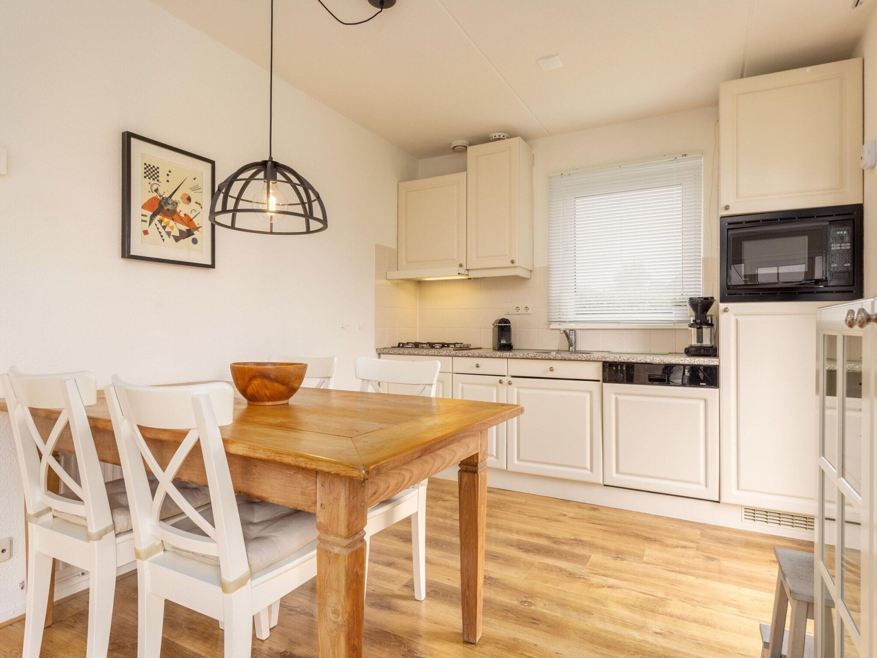 A modern kitchen with white cabinets, a wooden dining table, and a hanging light fixture.