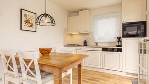 A modern kitchen with white cabinets, a wooden dining table, and a hanging light fixture. - Canal-side Bungalow Stay (Earnewald)