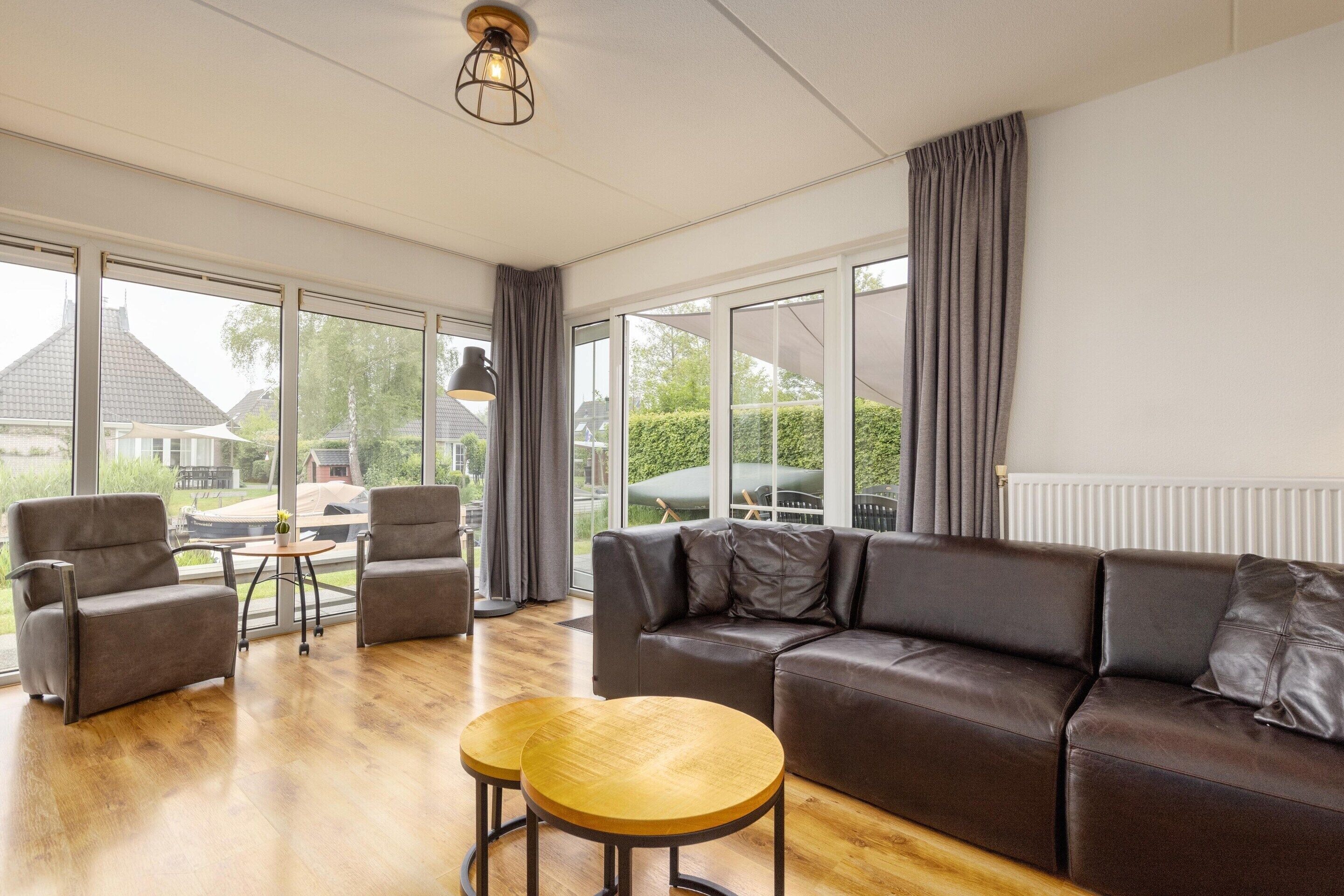 A modern living room with a leather sofa, two wooden side tables, and a view of the outdoors through large windows.