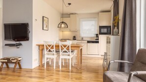 A compact living space with a kitchen, dining area, and a TV mounted on the wall. - Canal-side Bungalow Stay (Earnewald)