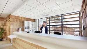 A reception desk with a wooden finish, a potted plant, and a view of a snowy landscape through large windows. - Chalet in La Clusaz With Spa & Ski Access (La Clusaz)
