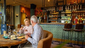 Un espace bar avec une table en bois, des chaises et un comptoir où sont exposées des bouteilles et des verres sur des étagères.