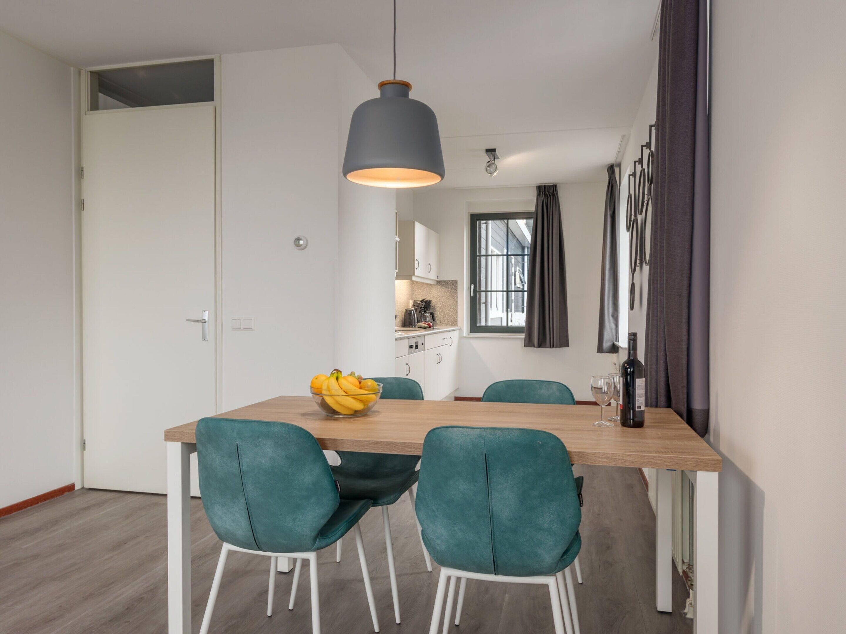 A modern dining area with a wooden table, teal chairs, a bowl of fruit, and a pendant light.