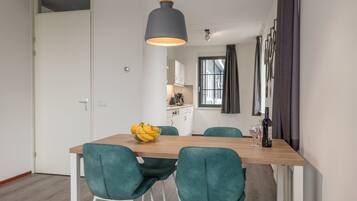 A modern dining area with a wooden table, teal chairs, a bowl of fruit, and a pendant light.