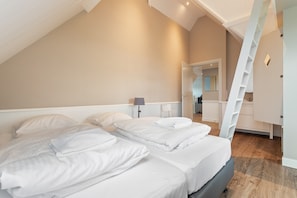 Een slaapkamer met twee bedden, een ladder, een spiegel en een deur naar een andere kamer.