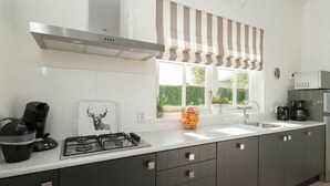 A modern kitchen with a gas stove, a coffee maker, and a sink. - Well-furnished Home With a Porch Near the Sea (Noordwijk)