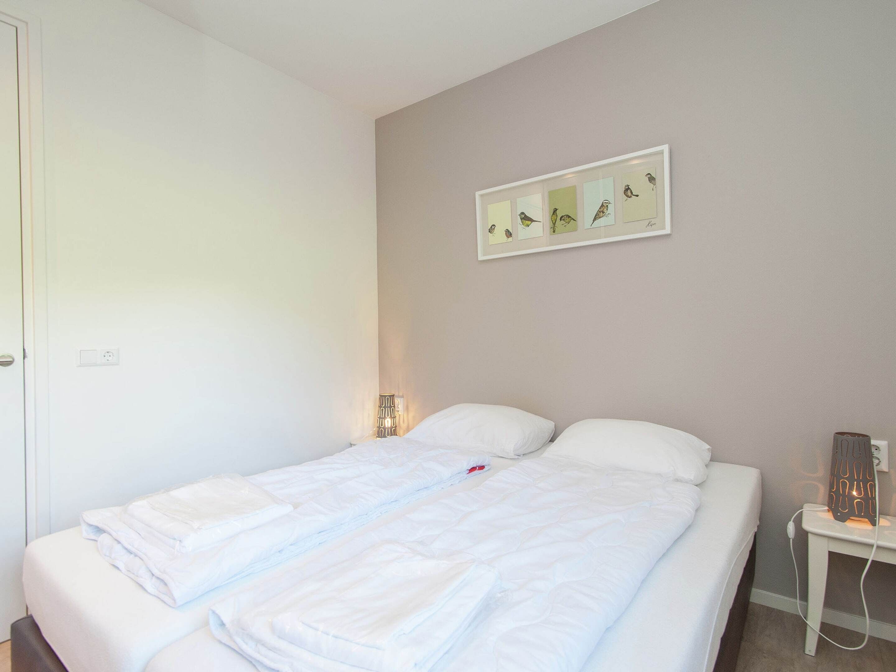 A neatly made bed with white linens, a bedside table with a lamp, and a wall-mounted artwork of birds.