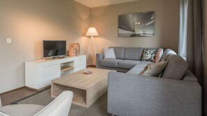 Ein modernes Wohnzimmer mit einem grauen Sofa, einem Couchtisch, einem Fernsehgerät auf einem weißen Schrank, einer Stehlampe und einem Gemälde an der Wand.