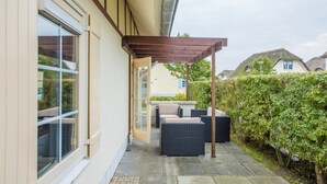 Eine überdachte Terrasse mit Gartenmöbeln, einem Steinweg und einer Hecke.