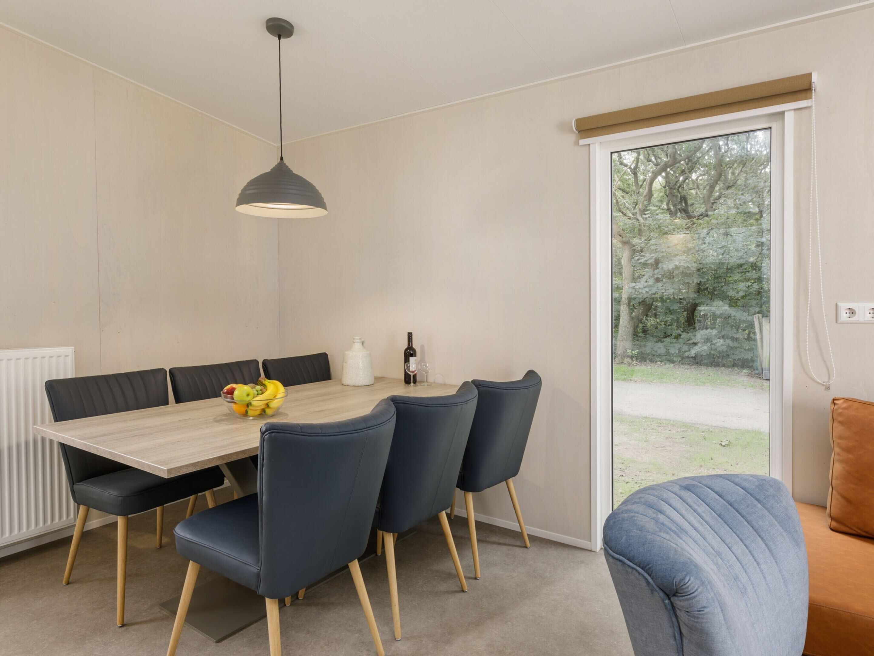 A modern dining area with a wooden table, dark blue chairs, and a hanging light fixture.