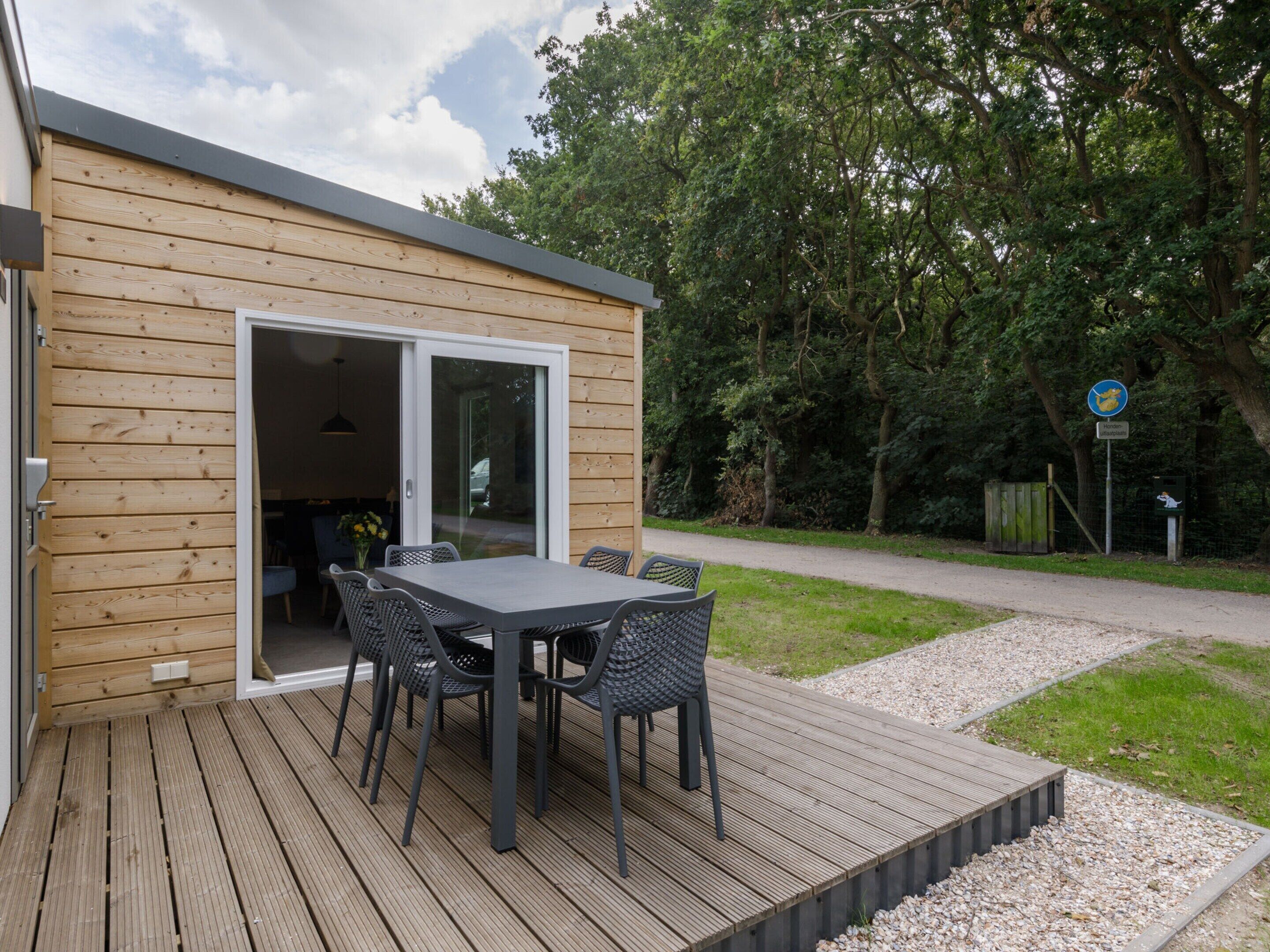 A wooden deck with a table and chairs, a sliding glass door, and a view of a wooded area.
