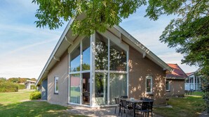 Une maison moderne dotée de grandes fenêtres en verre, d’une façade en briques et d’un patio aménagé avec du mobilier d’extérieur.