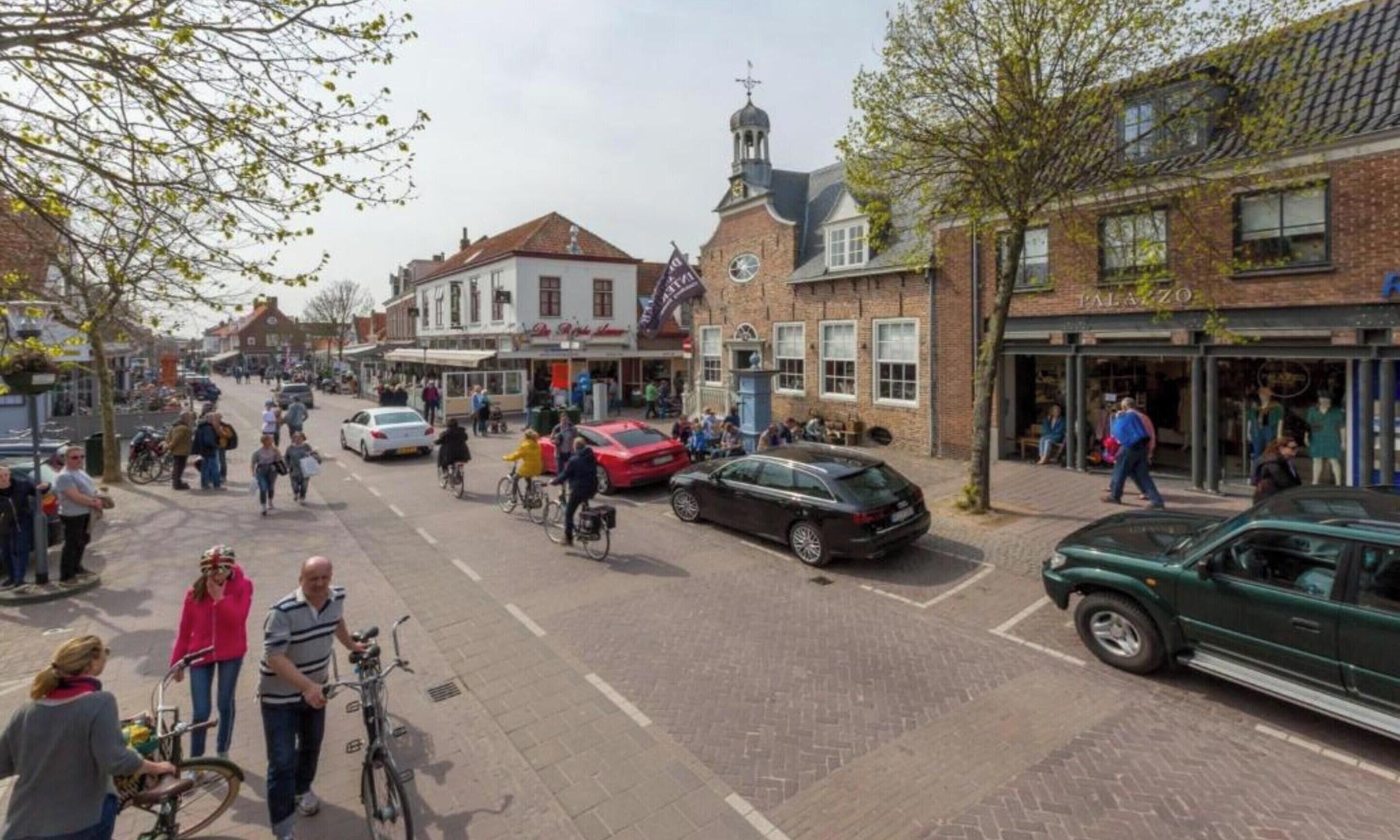 Straßenszene mit Fußgängern, Fahrrädern und Autos.