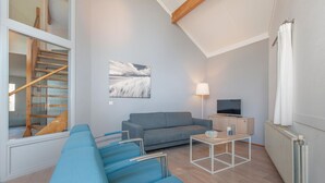 Un salon moderne avec un canapé gris, un divan bleu, un téléviseur et une lampe.