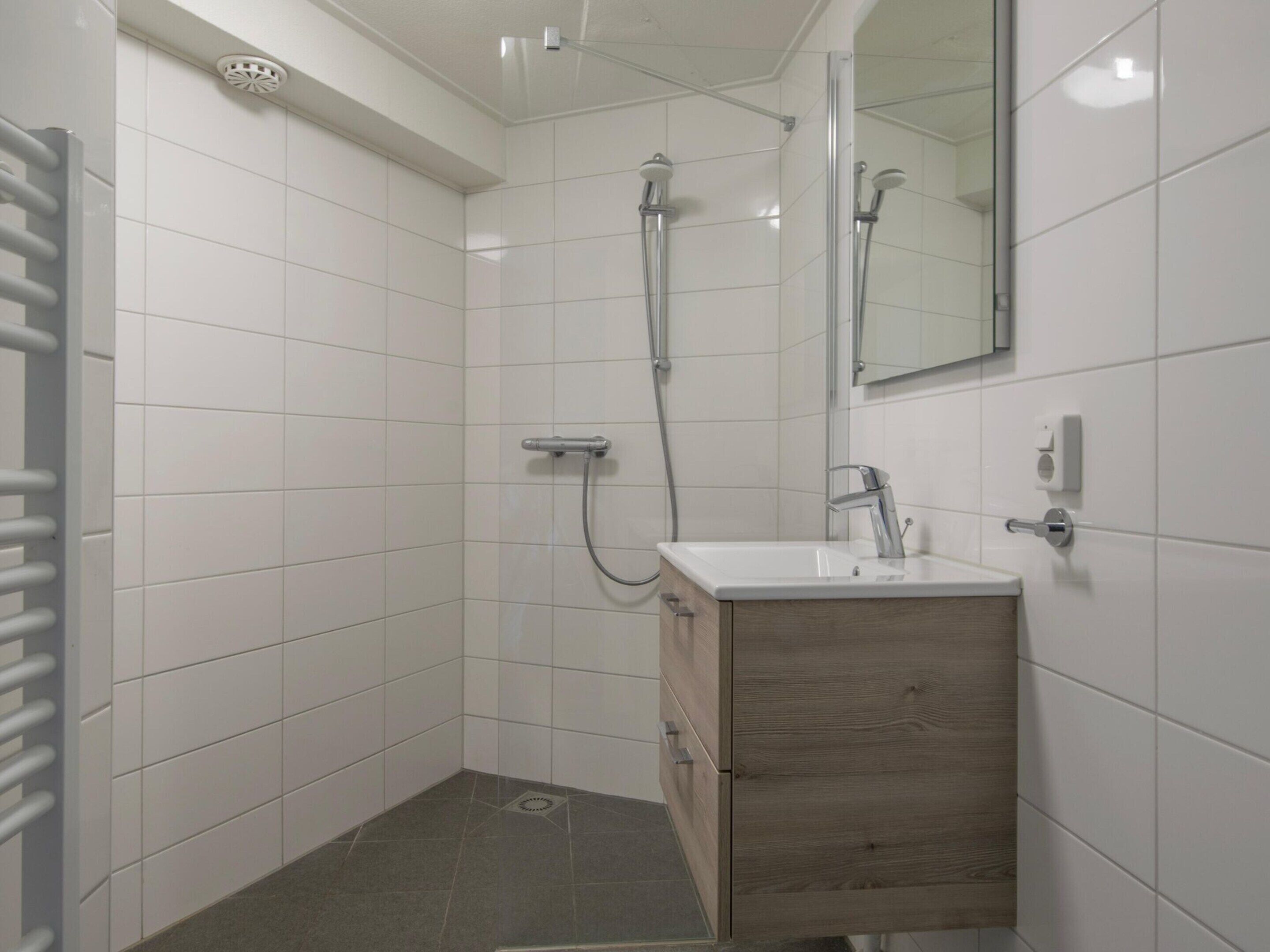 Ein modernes Badezimmer mit weißen Fliesen, einer Dusche, einem Waschbecken und einer Holzkommode.