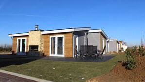 Una casa moderna amb una llar de pedra, un pati amb cadires i un cel blau clar.
