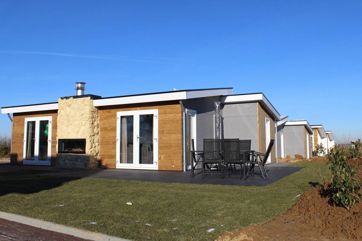 A modern house with a stone facade, large sliding glass doors, and a patio with outdoor furniture.