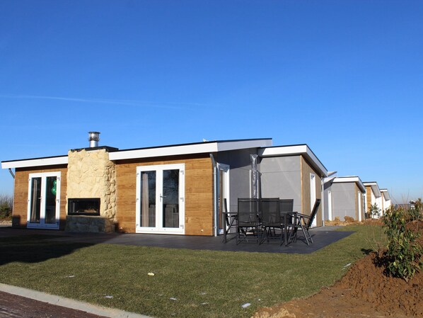 A modern house with a stone facade, large sliding glass doors, and a patio with outdoor furniture. - Stylish Villa in Bemelen (Bemelen)