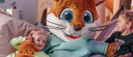 A person in a large, furry costume sitting on a bed with two children.