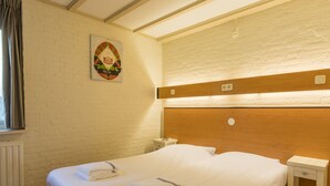 Un lit double avec du linge de lit et des serviettes blanches, une tête de lit en bois, une petite table de chevet et un radiateur.