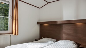 Une chambre avec deux lits simples, une tête de lit en bois, une fenêtre avec des rideaux et un radiateur.