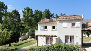 A two-story building with a tiled roof, a covered patio with chairs, and a garden with trees and shrubs. - Cozy Stay in Ardeche (Salavas)