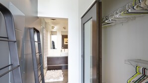 A hallway with a modern interior, a white fluffy rug, a metal drying rack, and a glass door leading to a bathroom. - East Nashville Condo | Rooftop + Parking | 30+ Days (Nashville)