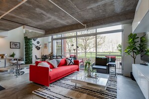 A modern living room with a red sofa, a coffee table, and a large window offering a view of the outdoors.